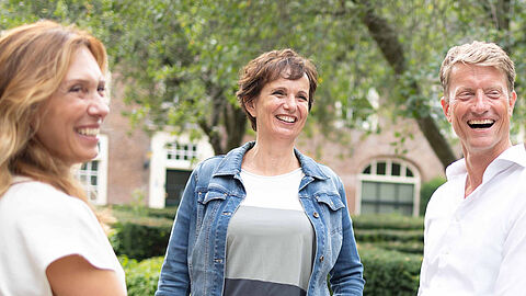 Drie collega's poseren in tuin en lachen